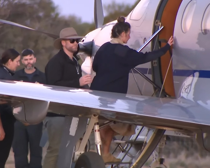 Backpacker found after going missing in Australian outback, boarding a small aircraft with support team nearby.