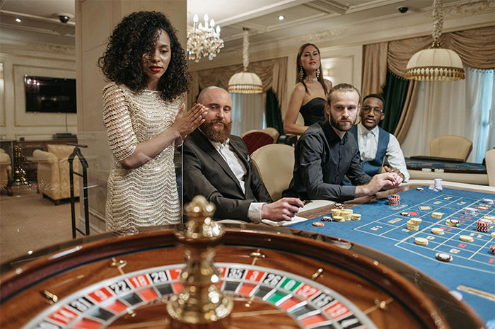 Casino workers and players engaging around a roulette table in an elegant casino setting.