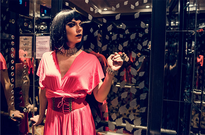 Woman in a pink dress with dark hair inside a casino elevator reflecting stories of casino workers and their experiences.