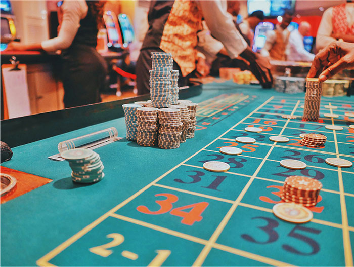 Casino workers handling chips and bets at a roulette table inside a busy casino floor environment.