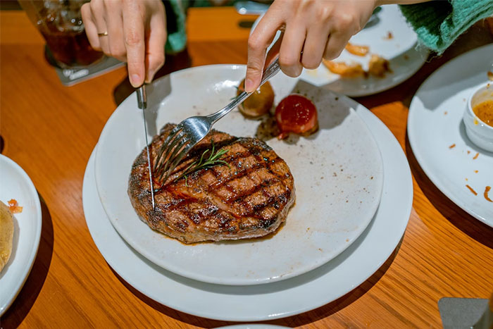Person cutting a grilled steak on a white plate, illustrating moments shared by casino workers in heartfelt stories.