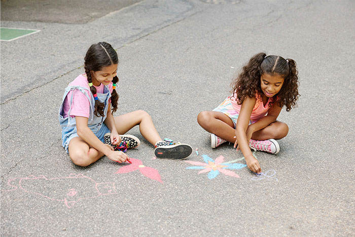 Two young girls drawing colorful chalk art on pavement representing creativity and stories from casino workers.