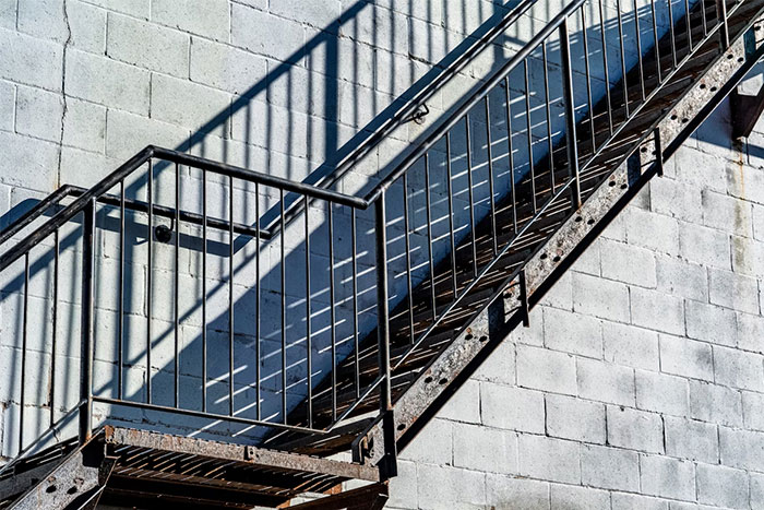 Rusty metal staircase casting shadows on a concrete wall, symbolizing 90 casino workers sharing craziest and heartbreaking stories.