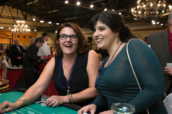 Two casino workers in stylish outfits sitting by slot machines, sharing moments in a dimly lit casino environment.
