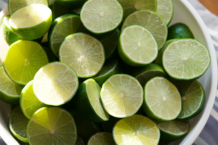 Bowl of fresh lime halves with bright green skin and juicy pulp, highlighting vibrant natural textures and colors.