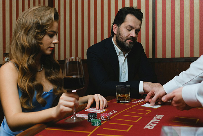 Casino workers dealing cards at a table with chips, drinks, and players in a lively gambling environment.