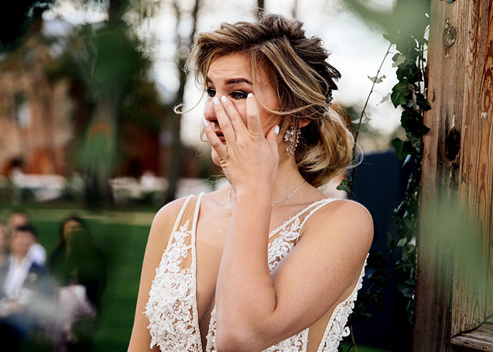 Bride in wedding dress wiping tears outdoors, reacting to caterers getting the wedding date wrong just before the ceremony.