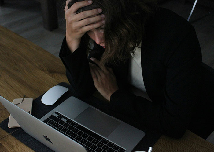 Woman stressed and upset sitting at a desk using laptop, reacting after bride finds out caterers got the wedding date wrong.