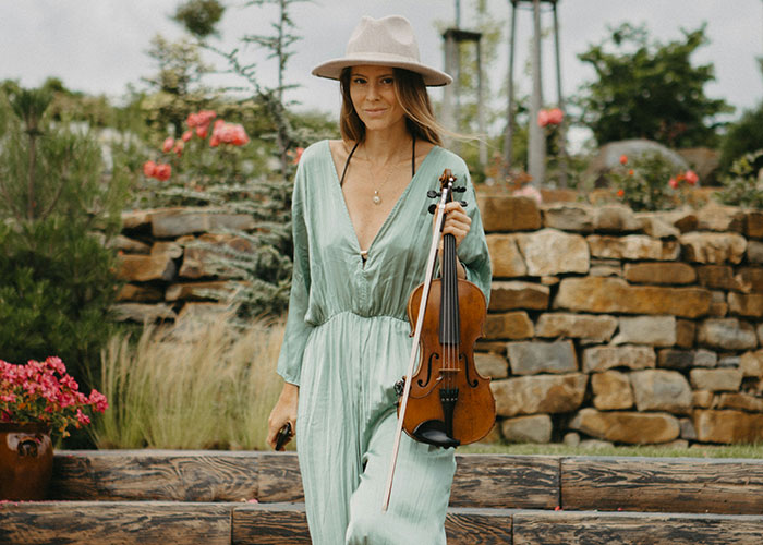 Woman in a green dress and hat holding a violin outdoors, symbolizing a bride facing unexpected wedding caterer issues.