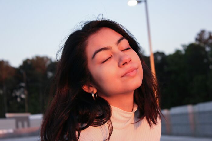 A young woman with eyes closed enjoying sunlight outdoors, representing people share things improved life and positivity. - 30
