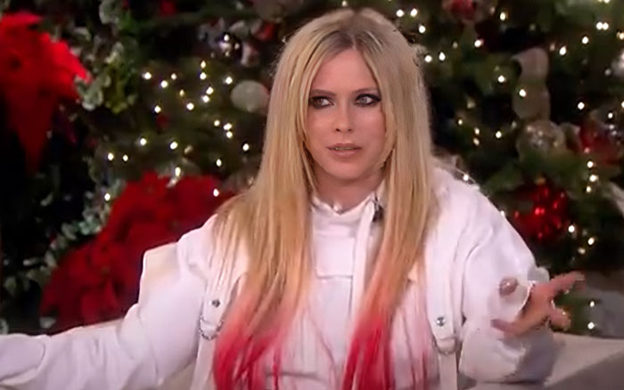 Blonde woman with red-tinted hair wearing a white jacket, speaking in front of holiday-themed decorations about celebrity breakup actions. - 18