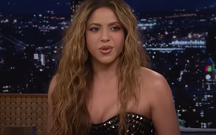 Singer with long wavy hair wearing a black strapless top during a late-night talk show about celebrity breakups. - 6