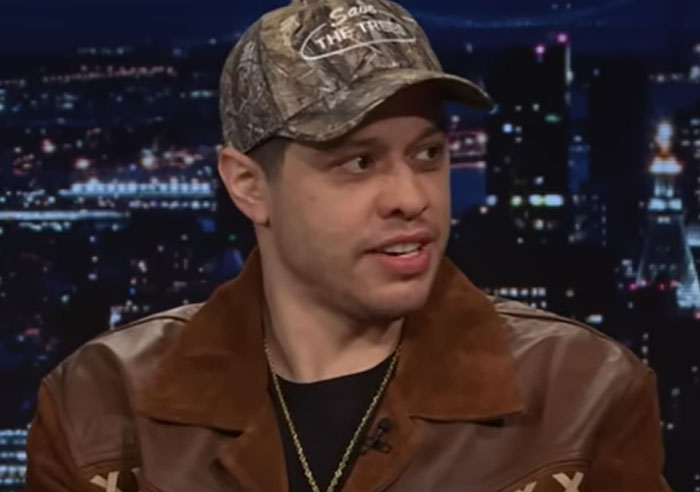 Man wearing a camouflage cap and brown jacket during a late night interview about wild things celebrities have done after a breakup - 26