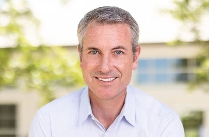 Smiling man outdoors wearing a light blue shirt, related to CEO comments about HR chief amid Coldplay scandal investigation.