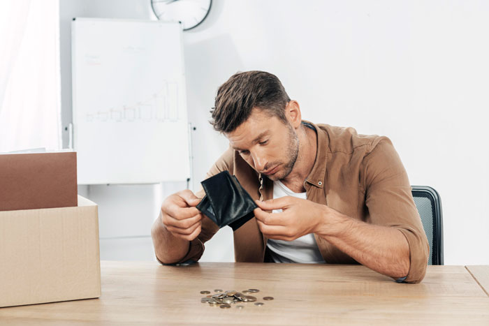 Man sitting at desk, looking into empty wallet with coins scattered, symbolizing nonexistent money issues. - 5