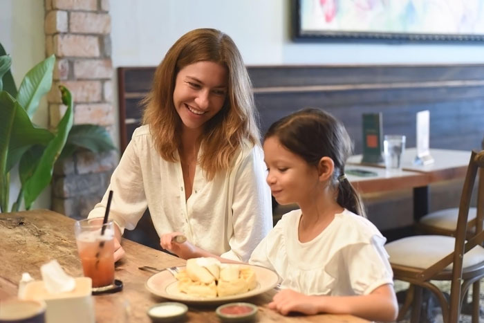 A smiling mom and her 8-year-old girl enjoying food together at a cozy cafe, talking and bonding.