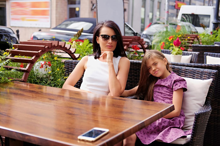 8YO girl sitting with her mom at outdoor caf&eacute;, both relaxed, enjoying time together in a casual urban setting.