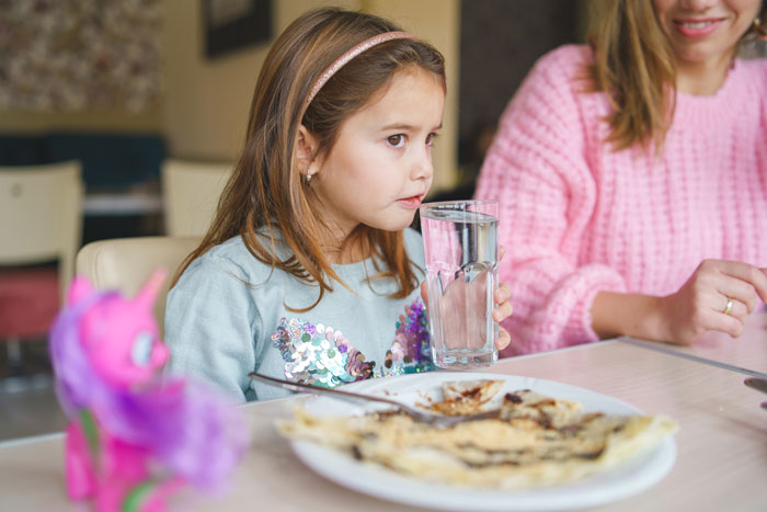 8-year-old girl sitting with her mom at a table, drinking water and eating food in a casual dining setting.