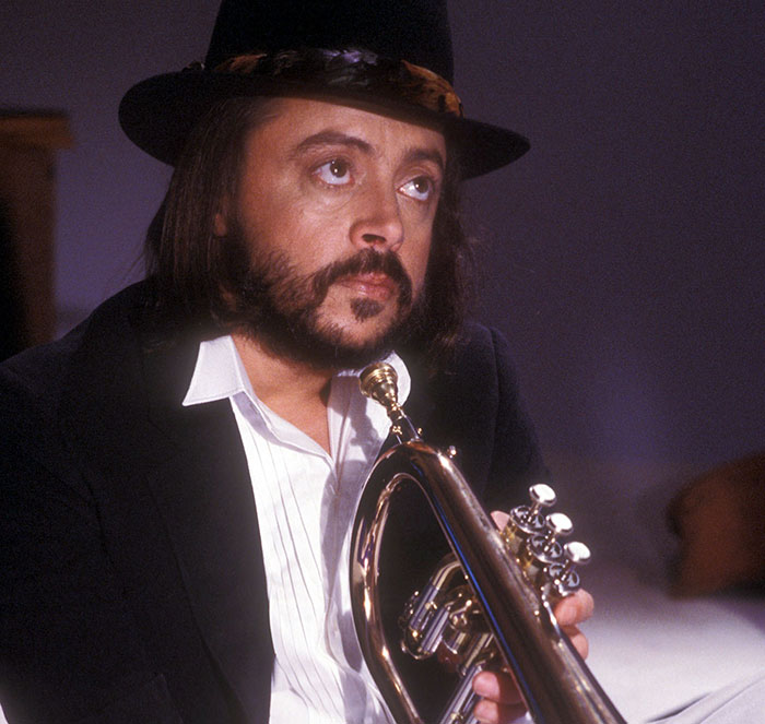Male musician wearing a black hat holding a trumpet, representing stars we lost this year in the entertainment industry.