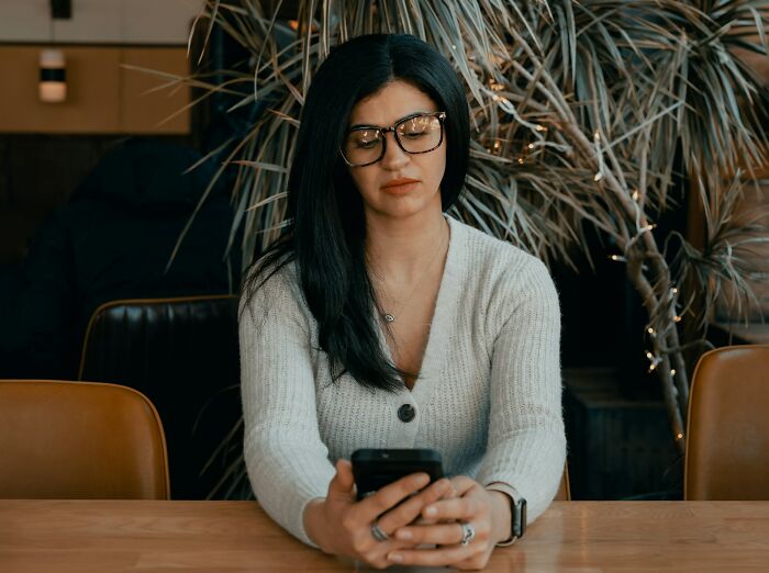 Woman with glasses and dark hair sitting at a table using smartphone representing private investigator weird cases insights - 8