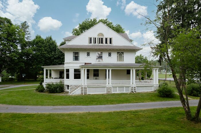 Large white historic house with wraparound porch surrounded by green trees and lawn, travelers share surprising things about U.S.