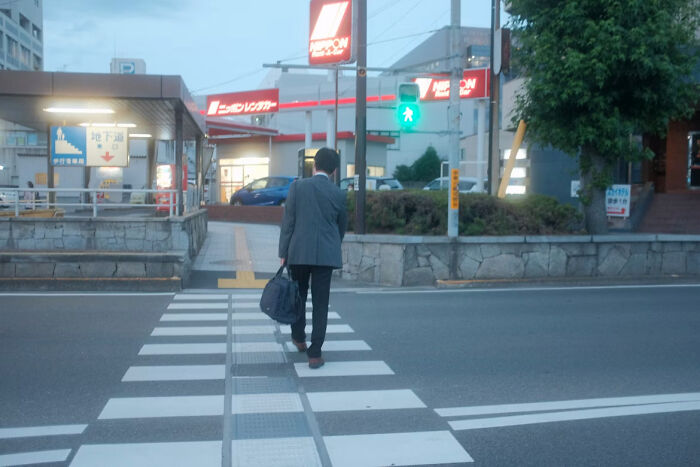 Man in business attire walking across a quiet crosswalk at dusk, illustrating things normal to men but bizarre to women.