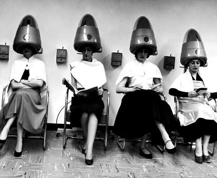Four women sitting under vintage hair dryers in a salon, a unique old photo capturing a moment from the past.