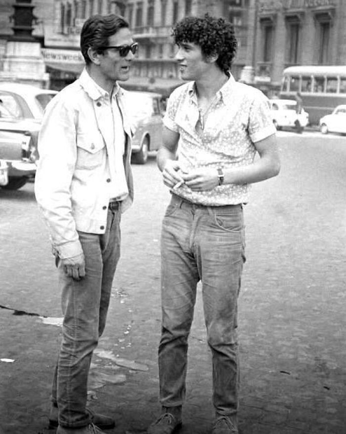 Two men in casual 1970s clothing having a conversation on a street in a unique old photo.