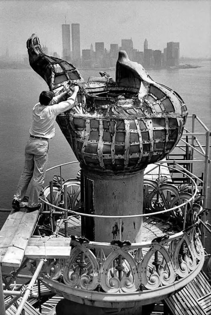 Man repairing the torch of the Statue of Liberty with New York City skyline in the background, unique old photo.