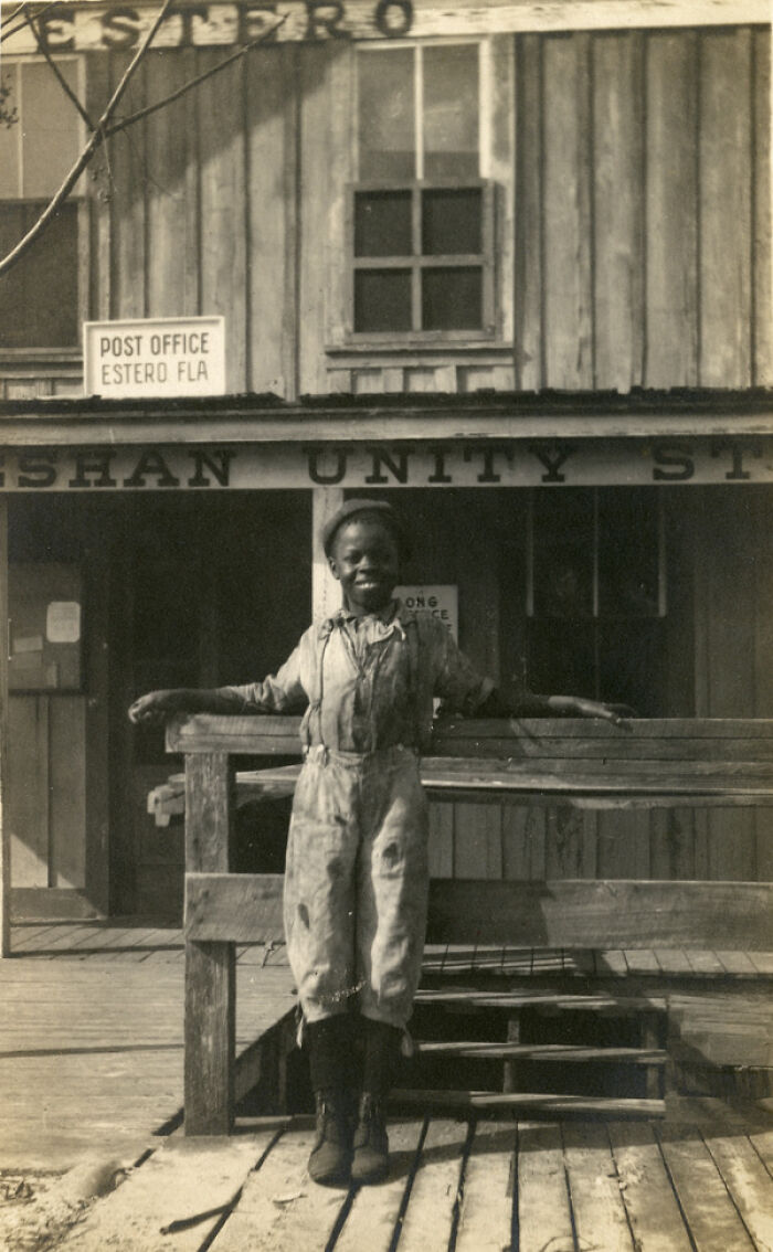 Young boy smiling while standing on porch outside post office in a unique old photo with an incredible story behind it
