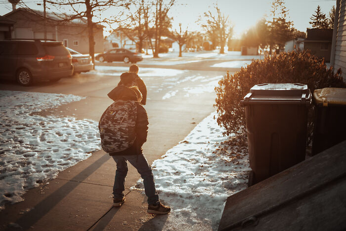 Two children walking on a snowy sidewalk during sunset in a residential neighborhood, evoking eerie real-life moments.