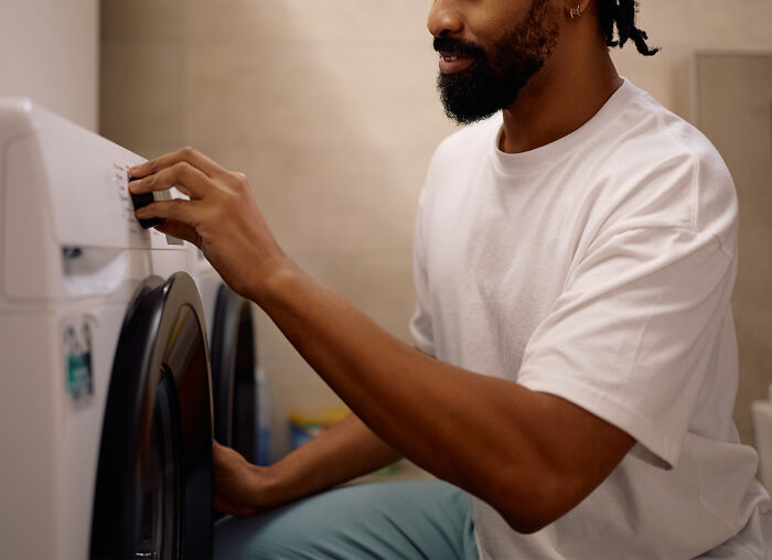 Person in a white shirt adjusting washing machine settings, illustrating real creepy things people have witnessed or heard about.