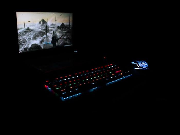 Gaming keyboard and mouse with colorful lights in dark room, screen showing eerie scene related to creepy real stories.