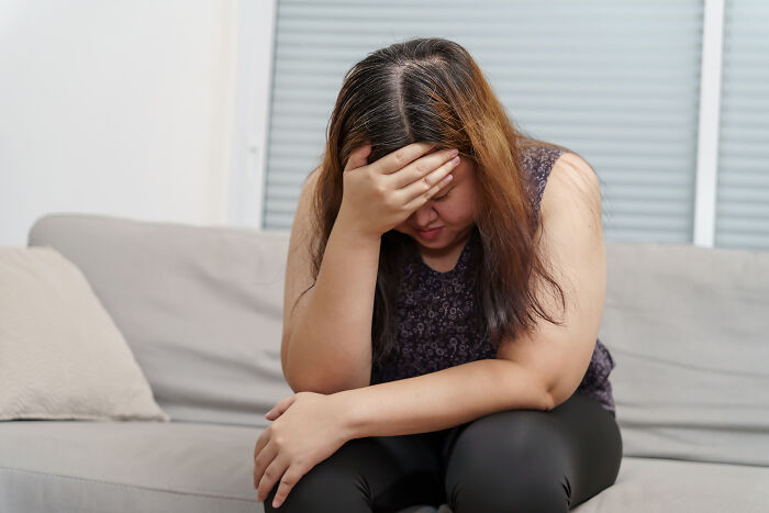 Woman sitting on couch with head in hand, appearing stressed and reflecting on creepy real things witnessed or heard about