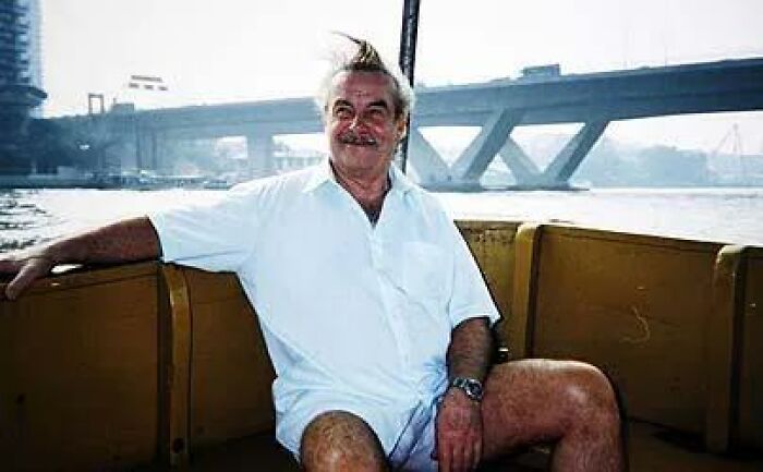 Man with white hair and mustache sitting on a boat with a bridge in the background, a photo with terrifying backstory. - 8