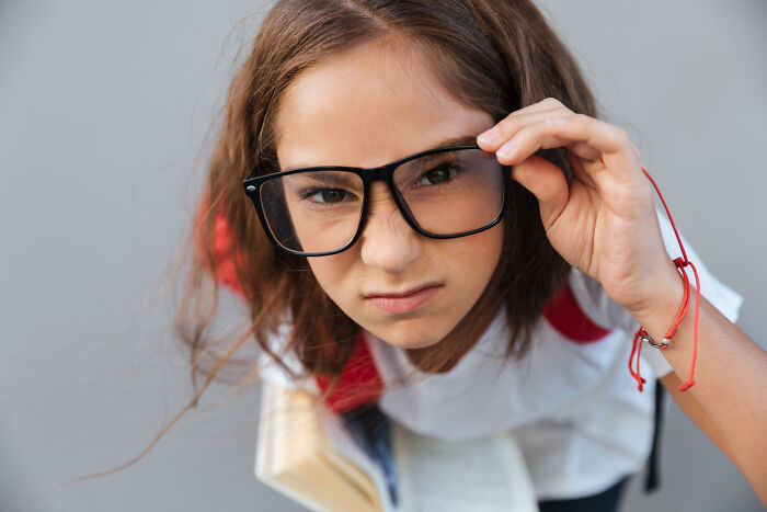 Young girl wearing oversized black glasses looking skeptical, illustrating impostor patients needing more common sense.
