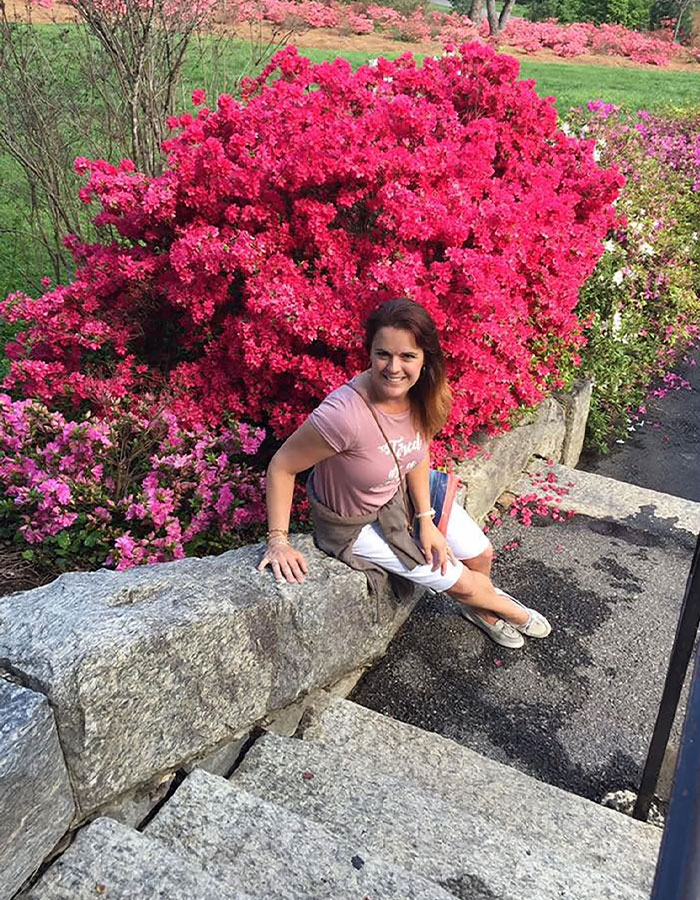 Woman sitting on stone wall near vibrant pink flowers in a garden, related to Colorado dentist lover red flags case. - 5