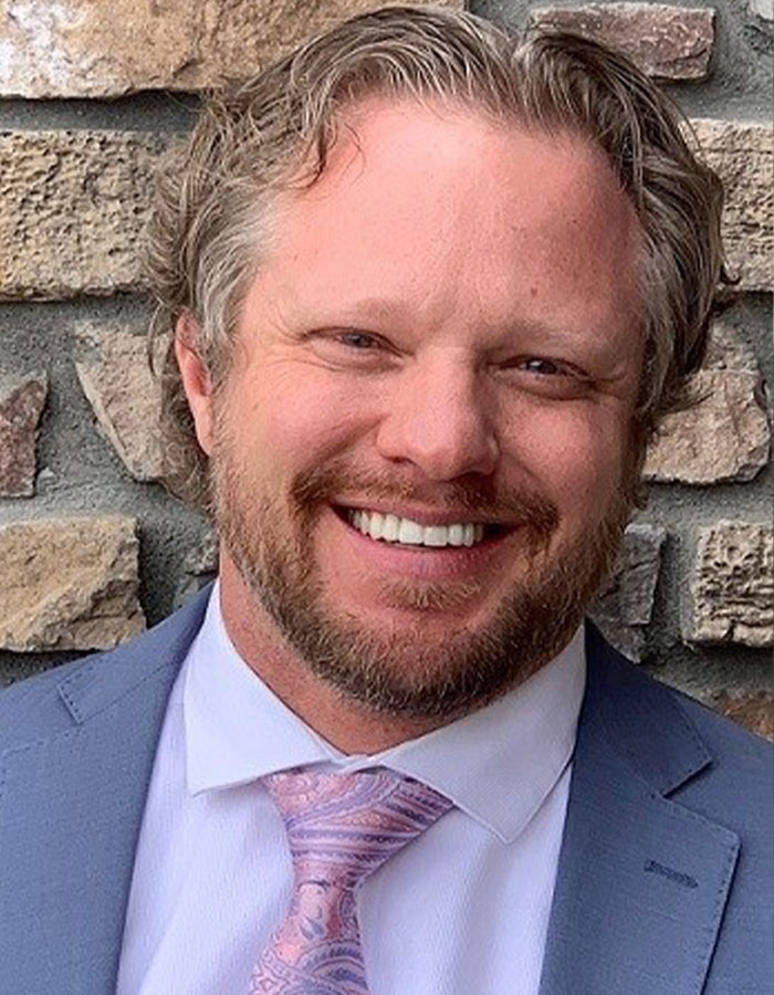Man smiling in suit and patterned tie against a stone wall, related to Colorado dentist lover and text messages case. - 8