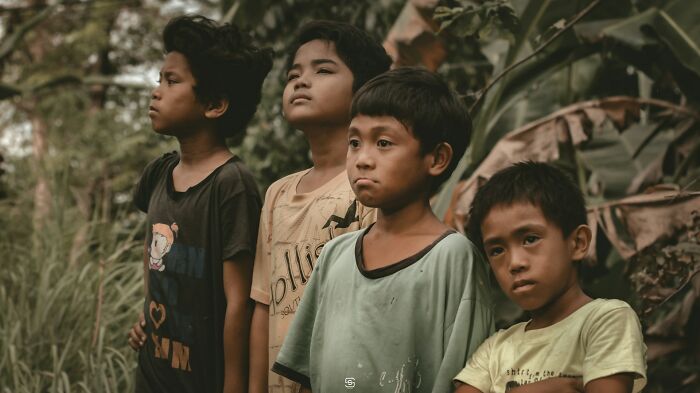 Four boys stand outdoors near greenery, representing diverse countries in a discussion about bizarre facts.