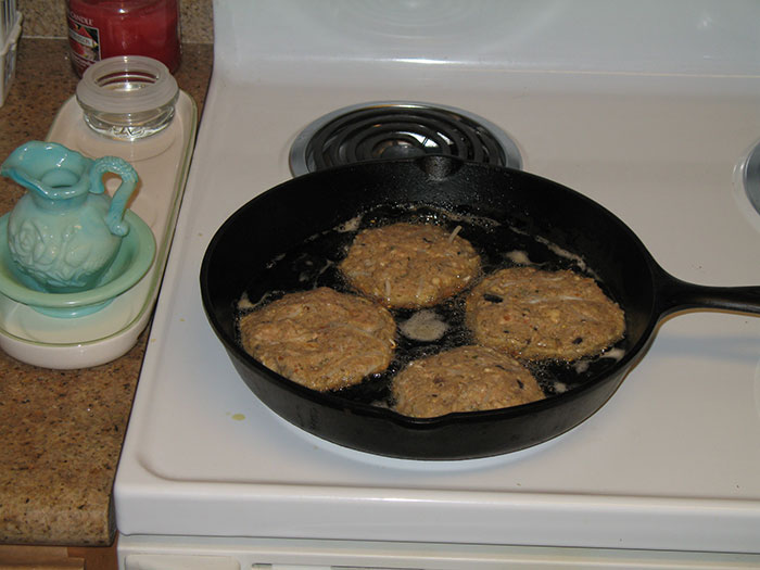 Frying patties in a cast iron skillet on a stove, related to washing chicken cooking myths discussion.