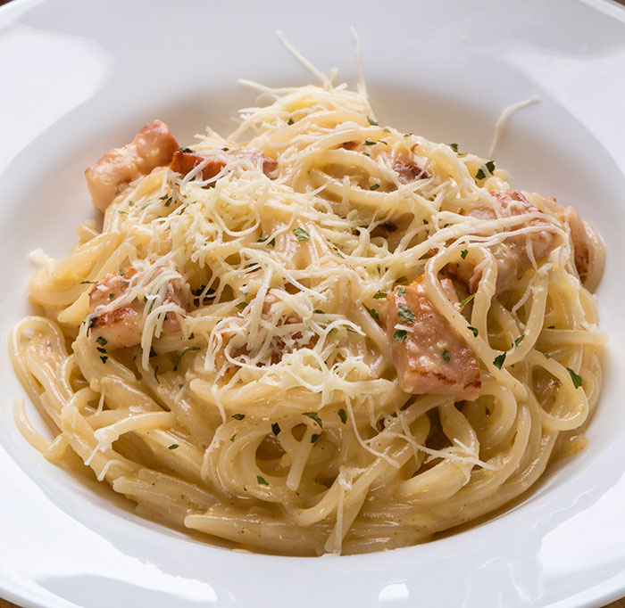 Plate of creamy pasta carbonara with grated cheese and pieces of cooked chicken, highlighting cooking myths about washing chicken.