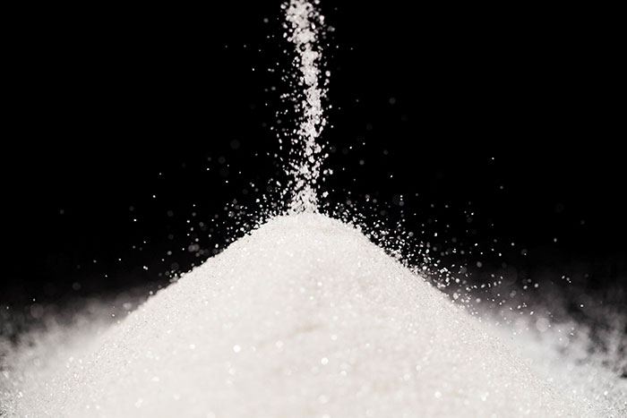 Close-up of granulated white salt pouring into a growing pile against a black background, illustrating cooking basics.