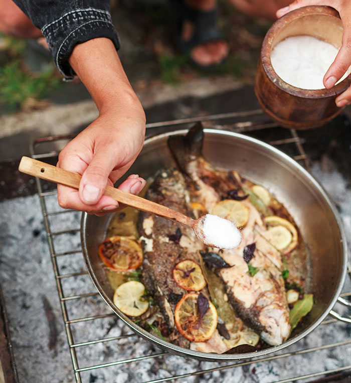 Person seasoning cooked fish with salt outdoors, illustrating key cooking practices beyond washing chicken myths.