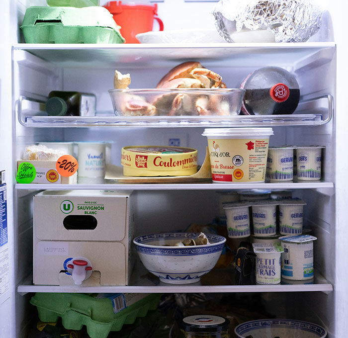 Open fridge with various food items including cheese, yogurt, eggs, and a bottle, illustrating cooking and food storage.