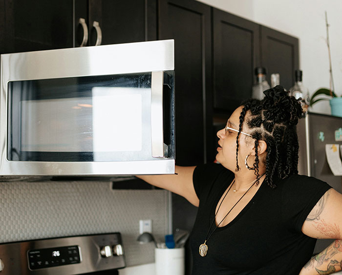 Woman in kitchen reaching for a microwave, representing washing chicken and debunking cooking myths in an online group.