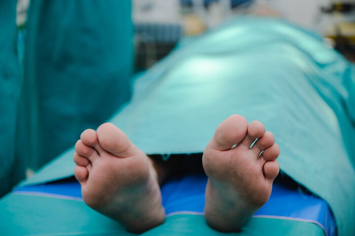 Bare feet of a body covered with a sheet on a morgue table, illustrating weird things uncovered by people who deal with dead bodies.