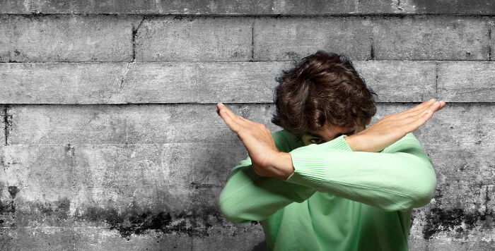 Person in green sweater making an X with arms against a concrete wall, showing people share things that improved life. - 20