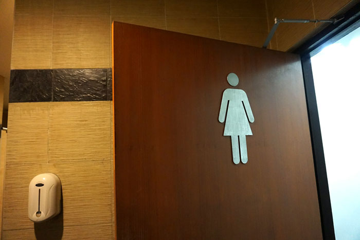 Women&rsquo;s restroom door with hygiene waste bin inside, highlighting custodian&rsquo;s refusal to empty bins due to religion.