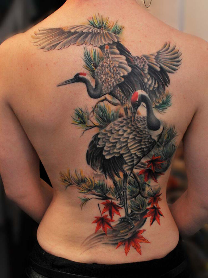 Detailed back tattoo of two cranes with pine branches and red leaves, showcasing one of the best tattoos with vibrant colors and fine details.