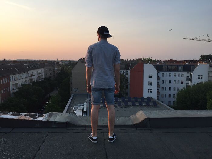 Young man standing on rooftop at sunset overlooking urban buildings, representing strange calls first responders encounter.